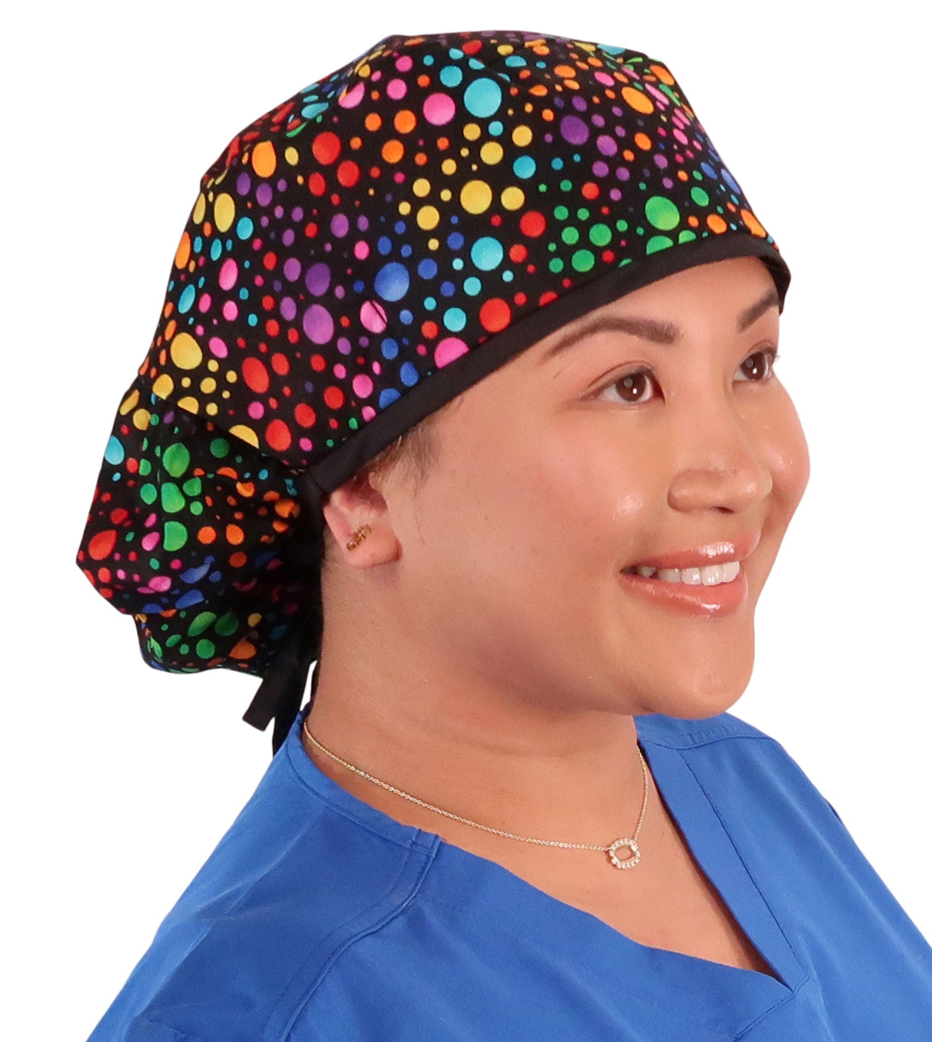 Front facing untied image of a woman in scrubs wearing a Big Hair Ponytail Scrub Cap with a Multi Color Dots pattern, and black ties to hold the scrub cap in place.