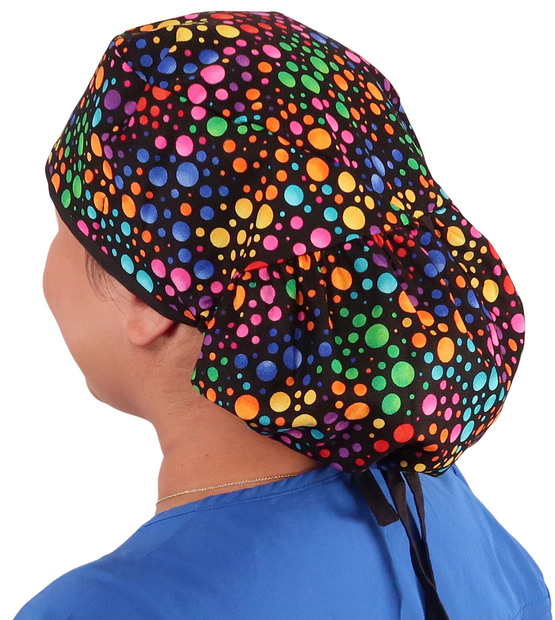 Side facing untied image of a woman in scrubs wearing a Big Hair Ponytail Scrub Cap with a Multi Color Dots pattern, and black ties to hold the scrub cap in place.