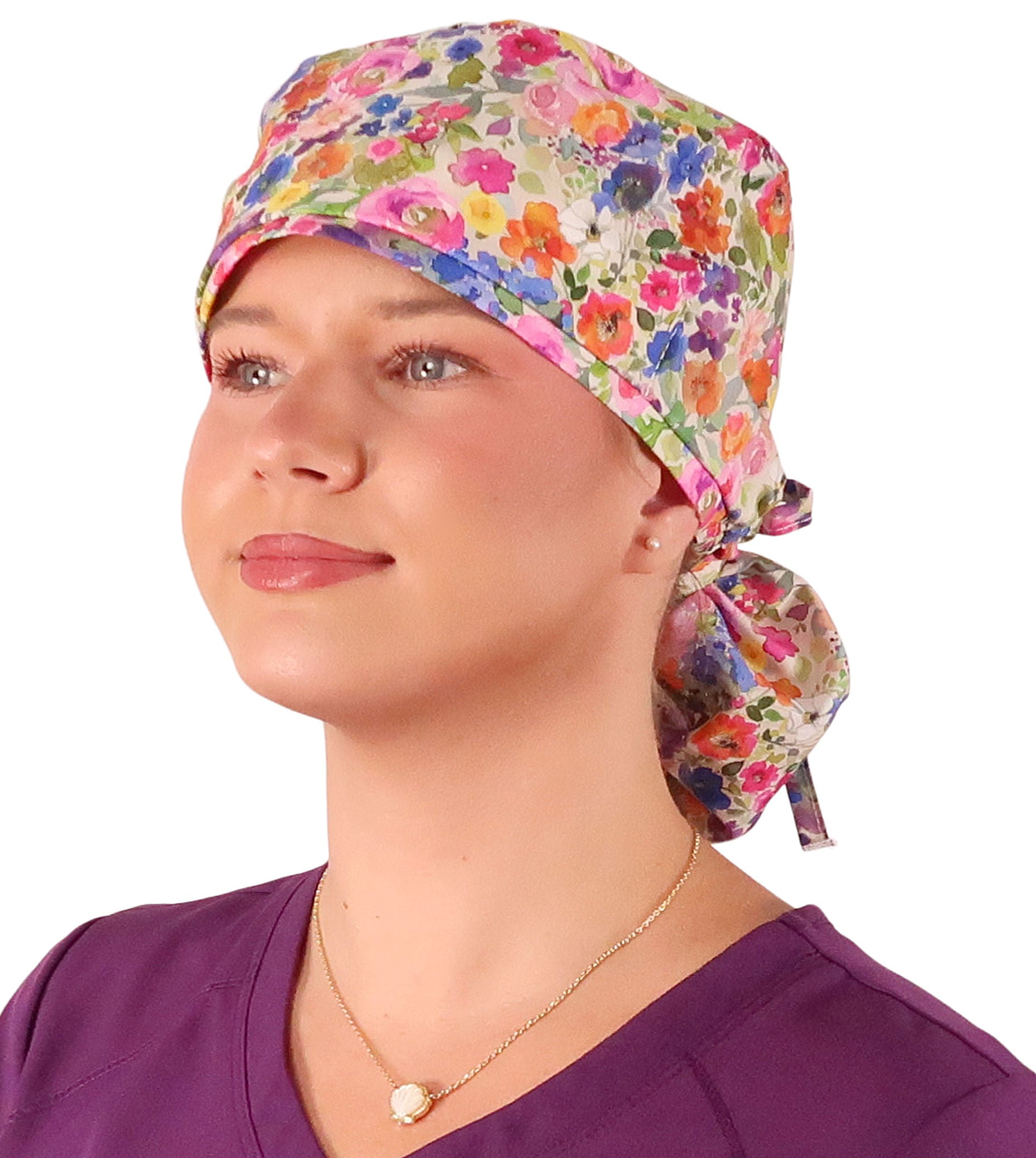 Front facing tied image of a woman in scrubs wearing a Big Hair Ponytail Scrub Cap with a Wondrous Wildflowers pattern.