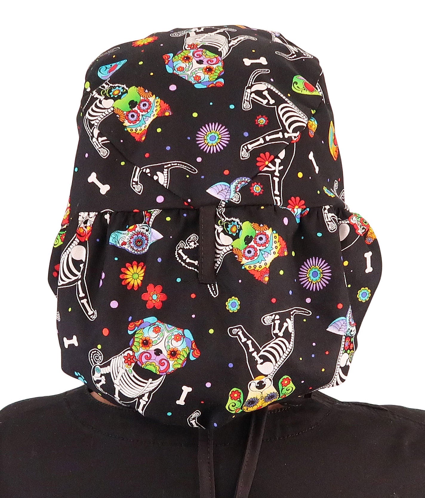 Back facing untied image of a woman in scrubs wearing a Big Hair Ponytail Scrub Cap with a X-Ray Dogs pattern, and black ties to hold the scrub cap in place.
