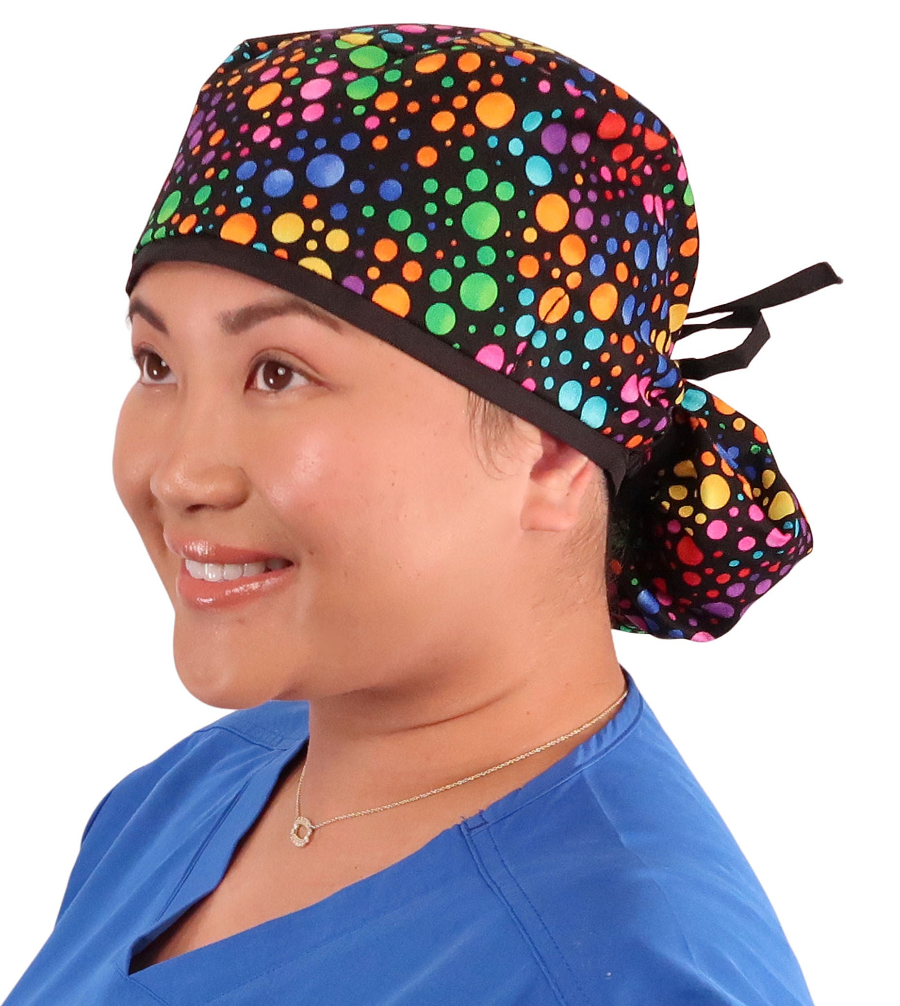 Front facing tied image of a woman in scrubs wearing a Big Hair Ponytail Scrub Cap with a Multi Color Dots pattern, and black ties to hold the scrub cap in place.