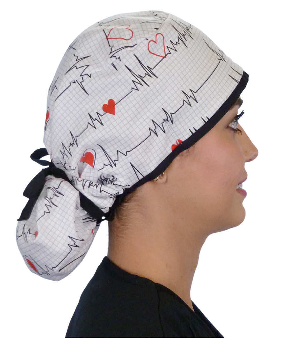 Side facing tied image of a woman in scrubs wearing a Big Hair Ponytail Scrub Cap with a Heartbeats on White pattern, and black ties to hold the scrub cap in place.