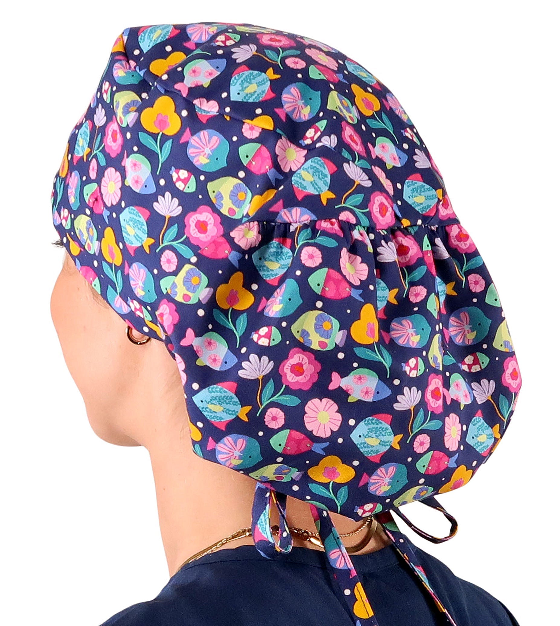 Side facing untied image of a woman in scrubs wearing a Big Hair Ponytail Scrub Cap with a Fabulous Fishies pattern.