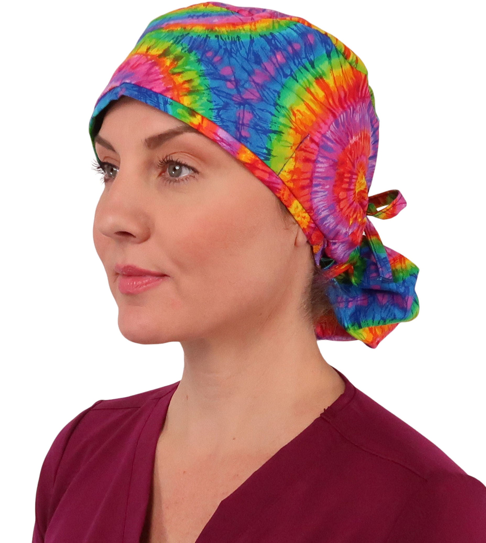 Front facing image tied of a woman in scrubs wearing a Big Hair Ponytail Scrub Cap with a Tie Dye pattern.